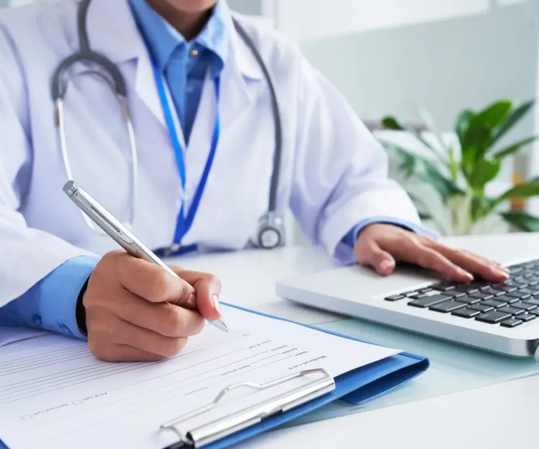 hands-of-unrecognizable-female-doctor-writing-on-form-and-typing-on-laptop-keyboard (1)