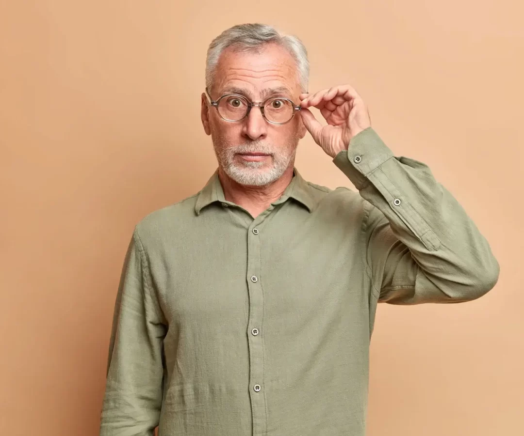 surprised-grey-haired-handsome-man-keeps-hand-on-rim-of-spectacles-hears-amazing-news-wears-formal-s (1)